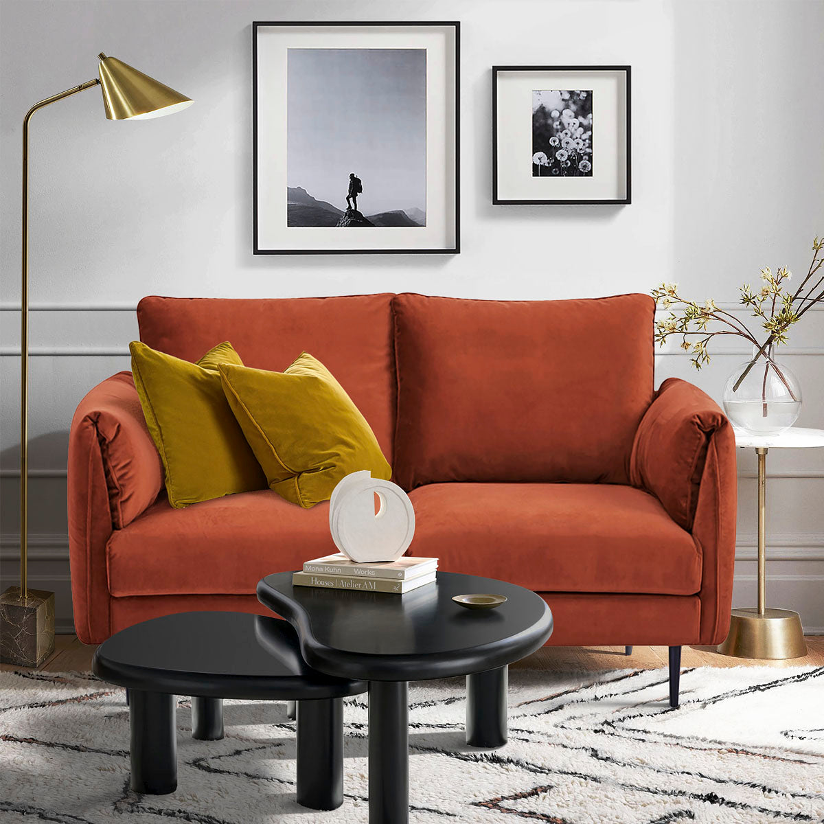Canapé 2 places en velours terracotta dans un intérieur moderne, décoré de coussins jaune moutarde, tables basses noires design, lampe dorée et tableaux muraux, ambiance chaleureuse et élégante.